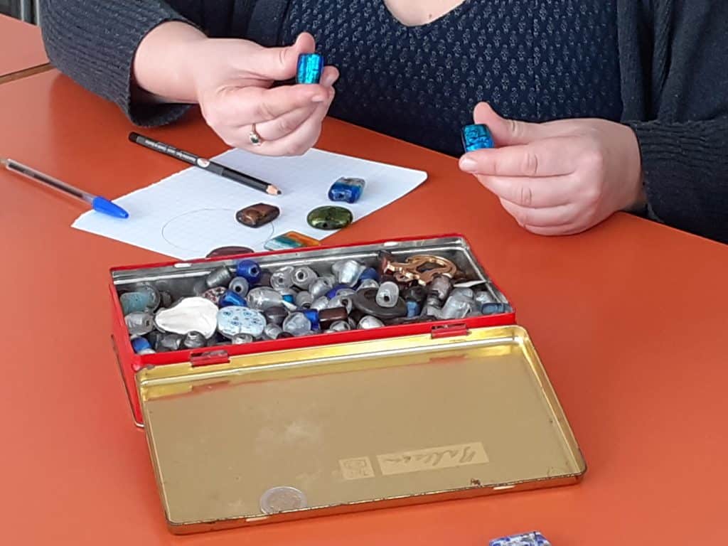 Feuille de papier et crayons posés sur une table, boîte ouverte contenant des perles mains tenant des perles