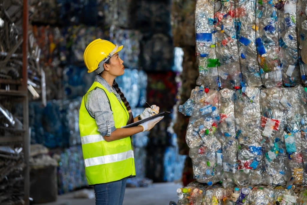 Femme avec casque de chantier devant une pile de balles de déchets triés et compactés